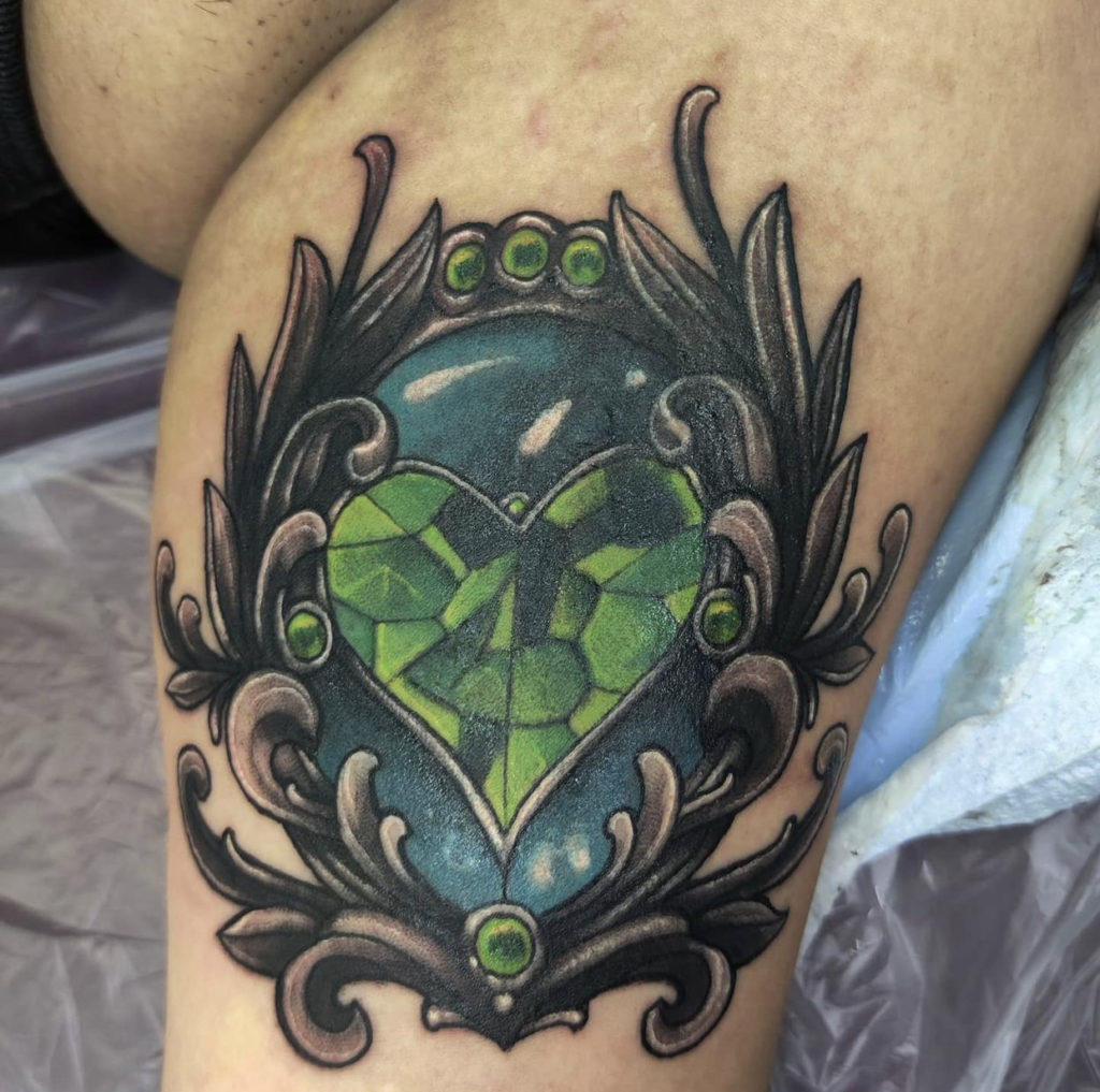 a cover-up tattoo of a green gem in front of a blue stone with black filigree by Mark Anthony at Artistic Impressions Tattoo Studio in Katy, Texas