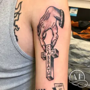 a tattoo of a hand holding a cross with the words “Black Sabbath”, by Colton at Artistic Impressions Tattoo Studio in Katy, Texas