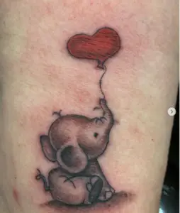a tattoo of a cartoon elephant holding a red heart balloon by Ulisses at Artistic Impressions Tattoo Studio in Katy, Texas