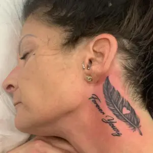 A feather tattoo on the neck with lettering by Ulisses at Artistic Impressions Tattoo Studio in Katy, Texas